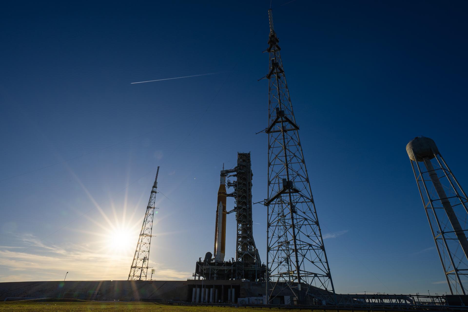The sun sets on NASA’s Space Launch System (SLS) rocket and Orion spacecraft as they stand fully assembled atop the mobile launcher at Launch Pad 39B at NASA’s Kennedy Space Center in Florida. The sky glows with warm shades of orange and pink, silhouetting the towering rocket and its solid rocket boosters against the fading light. Photographed on January 31, 2026, the scene captures teams preparing for a wet dress rehearsal for the Artemis II mission, rehearsing launch countdown timelines and procedures as day turns to night.